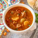 Tomato-based vegetable and meat soup in a white bowl.