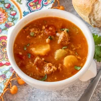 Tomato-based vegetable and meat soup in a white bowl.