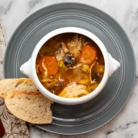 Creamy vegetable soup with carrots and celery, served in a white bowl on a gray plate, accompanied by slices of French baguette on a marble surface.