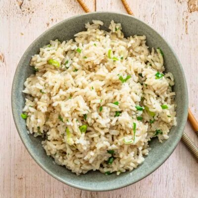 Steamed cauliflower rice with chopped green onions in a gray bowl.