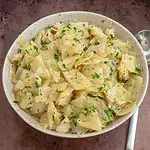 Bowl of mashed potatoes topped with chopped herbs and black pepper.