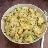 Bowl of mashed potatoes topped with chopped herbs and black pepper.