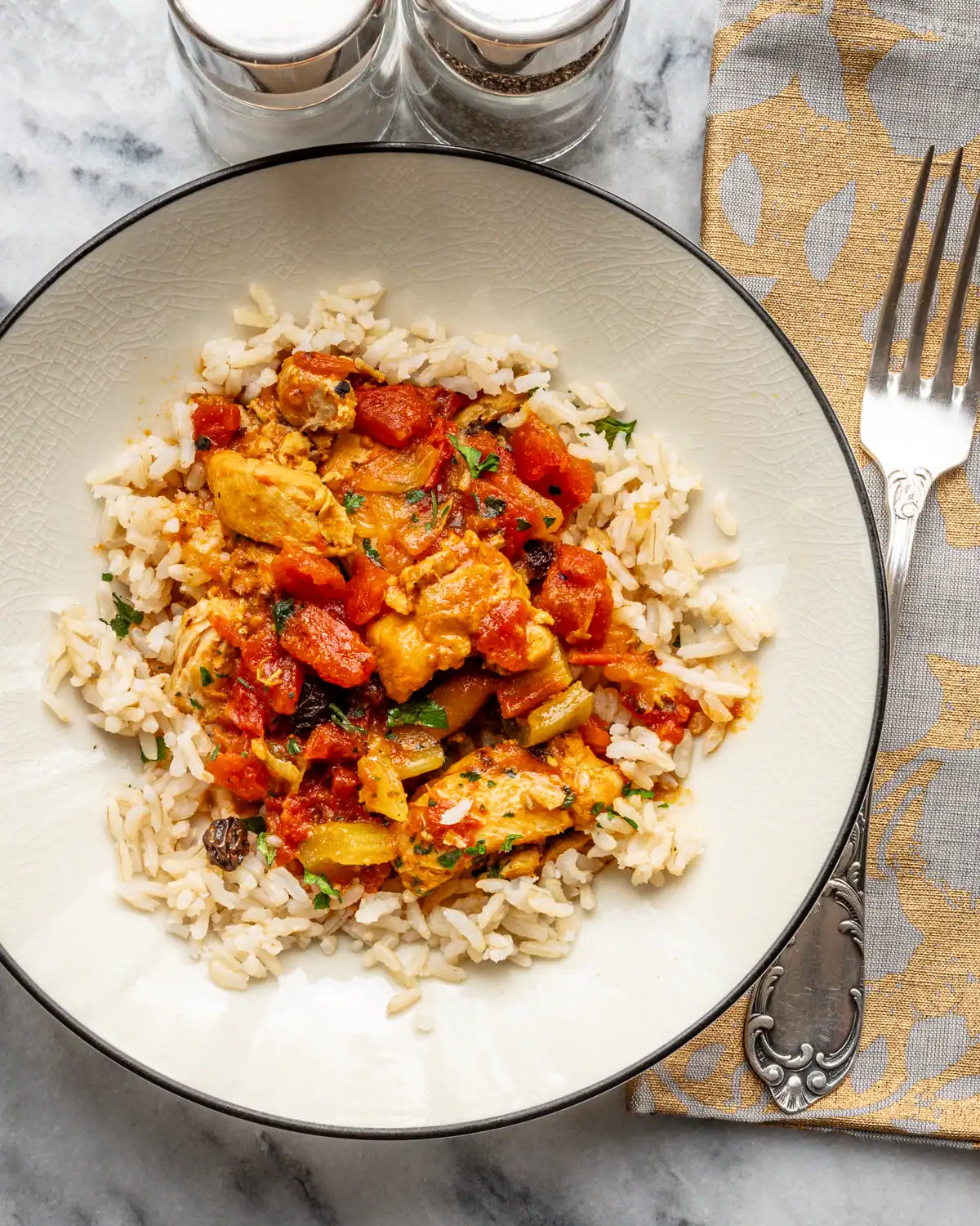 Savory chicken and vegetable stew served over white rice on a decorative plate.