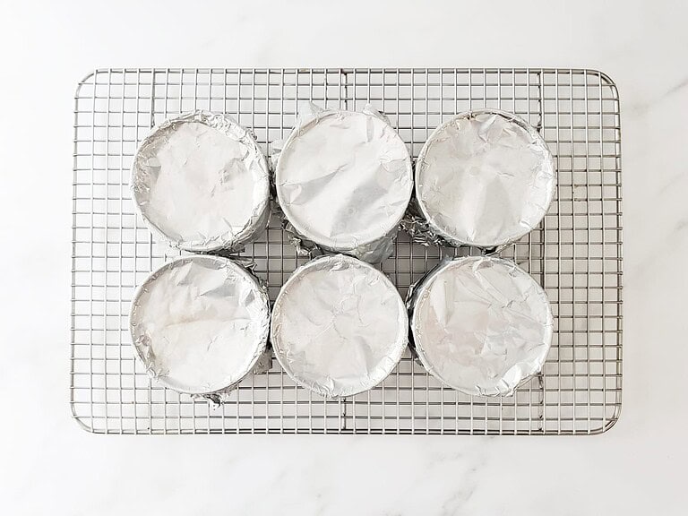 Baked cupcakes topped with foil wrappers, cooling on a wire rack.