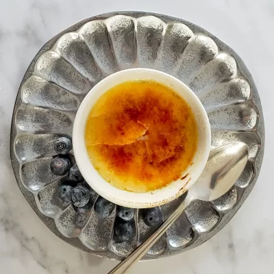 Creme brulee in a small white ramekin on a decorative silver plate with blueberries.