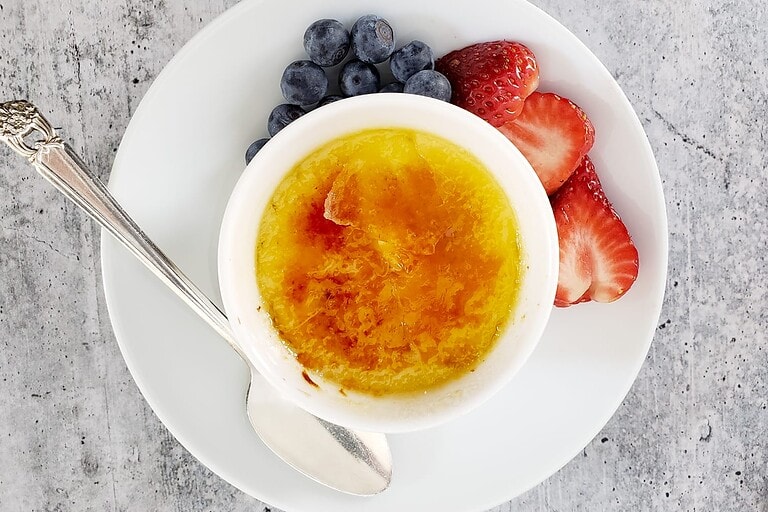 Fresh vanilla custard topped with caramelized sugar, served with blueberries and strawberries on a white plate.