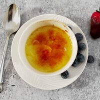 Baked custard in a white bowl with caramel topping and blueberries on the side.