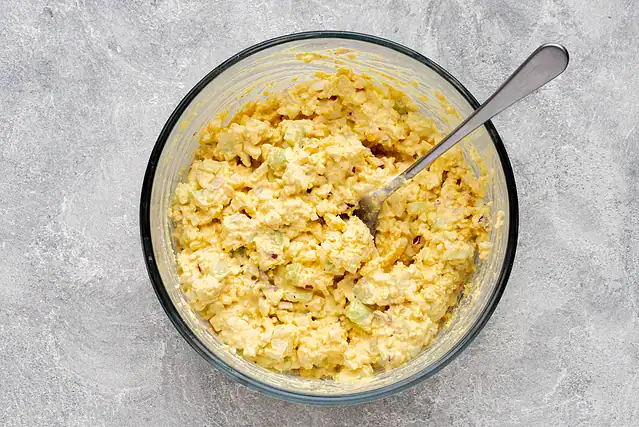Combining the egg yolks with seasonings and mayonnaise for deviled eggs.