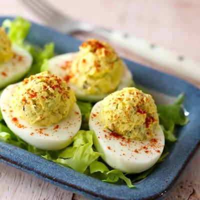 Deviled eggs garnished with paprika on a blue plate.