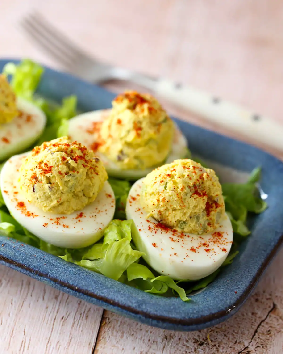 Deviled eggs garnished with paprika on a blue plate.