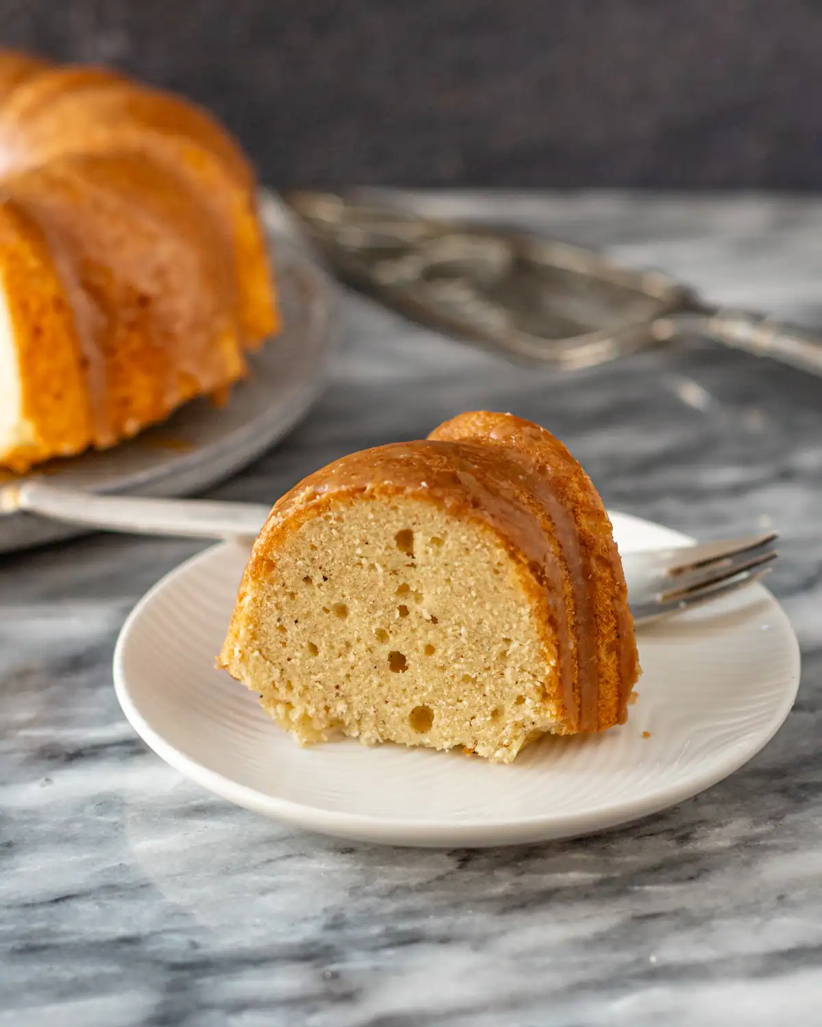 Fluffy vanilla cake slice with caramel glaze on white plate.