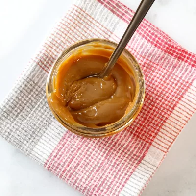 Creamy caramel spread in a glass jar with a metal spoon.