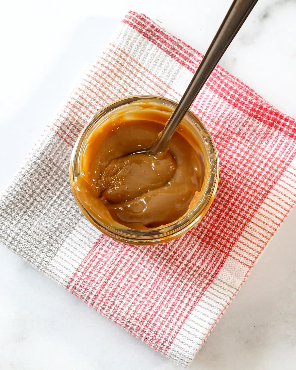 Creamy caramel spread in a glass jar with a metal spoon.