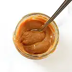 Creamy caramel sauce in a glass jar with a spoon inside.