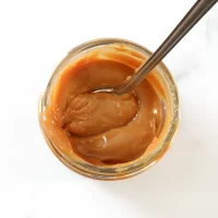 Creamy caramel sauce in a glass jar with a spoon inside.