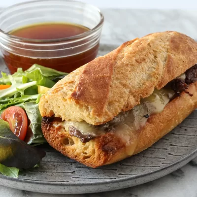 Crusty baguette sandwich with melted cheese and grilled meats on a gray plate.