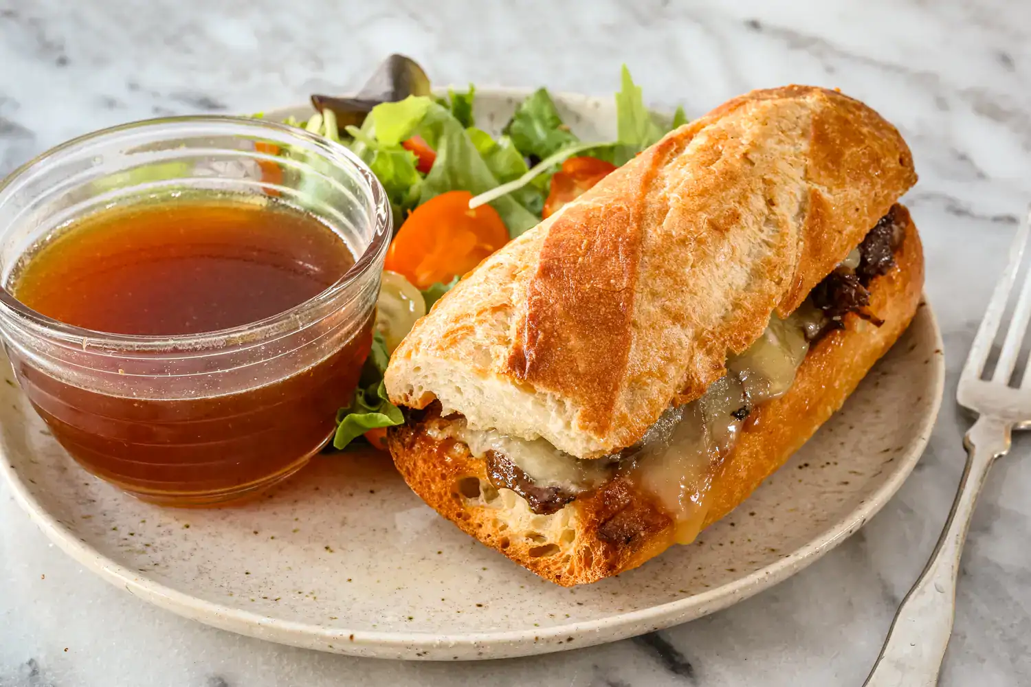 A French dip sandwich with jus and a side salad.