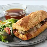 French baguette sandwich with melted cheese and beef patty on side salad.