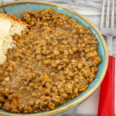 Bowl of cooked lentils with carrots and broth, with a piece of bread on the side.