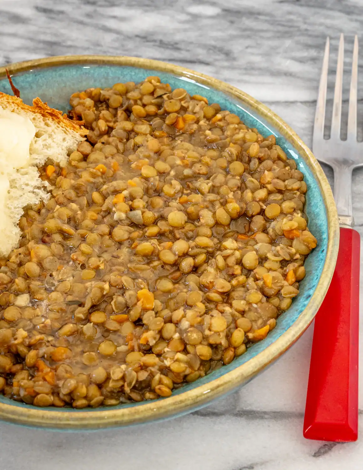 Bowl of cooked lentils with carrots and broth, with a piece of bread on the side.