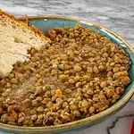 Bowl of cooked lentils with carrots and a slice of bread on the side.