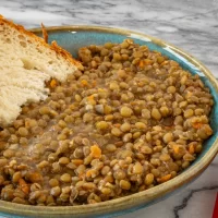 Bowl of cooked lentils with carrots and a slice of bread on the side.