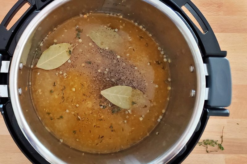 French lentils are ready to cook in the Instant Pot with bay leaves, the mirepoix, and seasonings.
