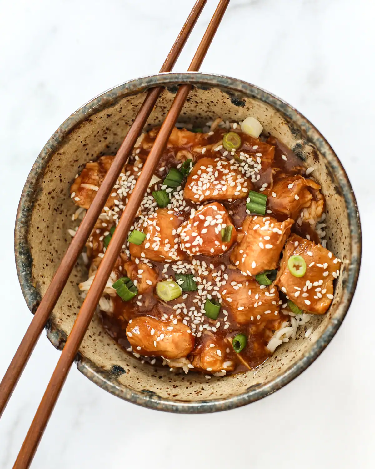 Fried chicken pieces topped with sesame seeds and chopped green onions in a bowl.