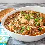 Savory chicken and mushroom stew garnished with green onions and sesame seeds in a white bowl.