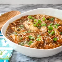 Savory chicken and mushroom stew garnished with green onions and sesame seeds in a white bowl.