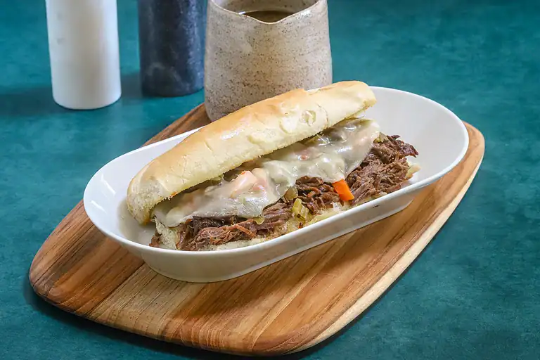 Slow-cooked shredded beef sandwich with melted cheese on a soft bun.
