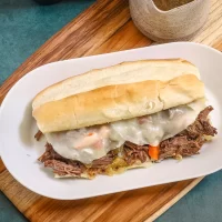 Shredded beef sandwich with melted cheese on a hoagie roll on a white plate.