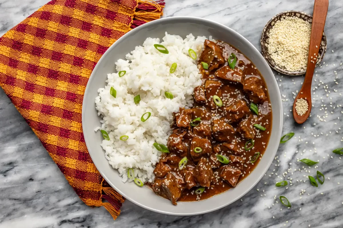 Savory beef stew served with fluffy white rice garnished with green onions.