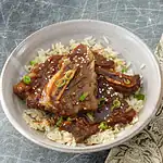 Braised short ribs on rice with green onions and sesame seeds.