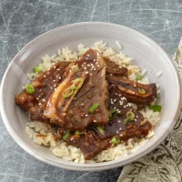 Braised short ribs on rice with green onions and sesame seeds.