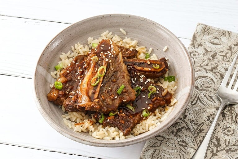 Braised short ribs served over rice with green onions and sesame seeds.