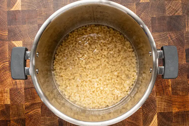 Boiled small pasta in a silver pot on wood surface.