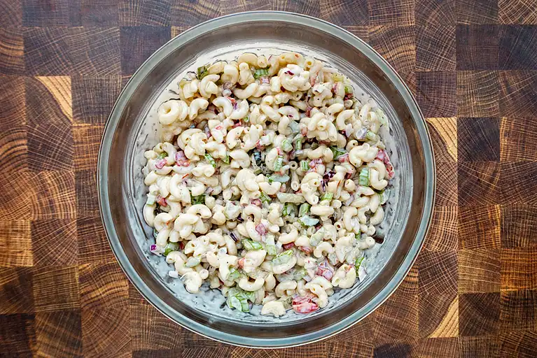 Creamy macaroni salad with chopped vegetables in a glass bowl.