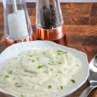 Creamy mashed potatoes garnished with chopped herbs, with salt and pepper shakers on a wooden table.