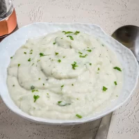 Creamy mashed potatoes garnished with chopped parsley in a white bowl.