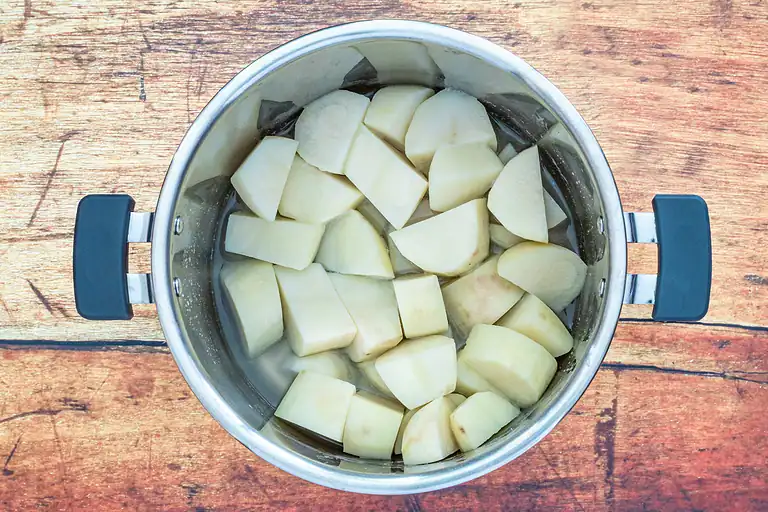 Sliced potatoes in a stainless steel pot filled with water.