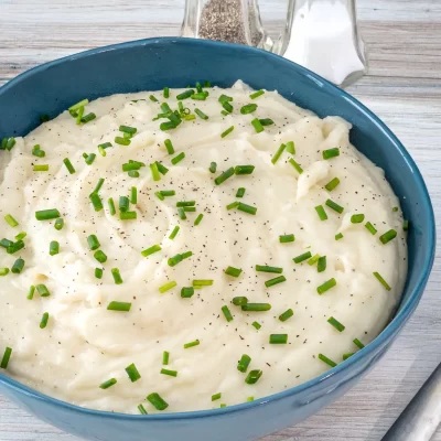 Creamy mashed potatoes garnished with chopped chives and black pepper.