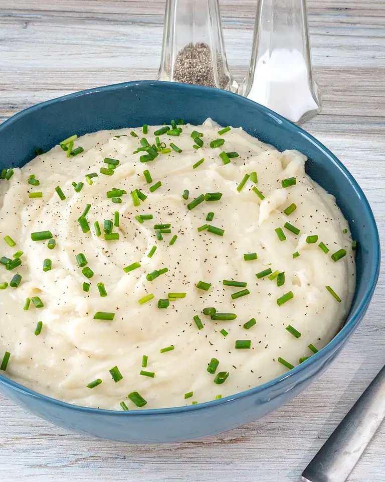 Creamy mashed potatoes garnished with chopped chives and black pepper.