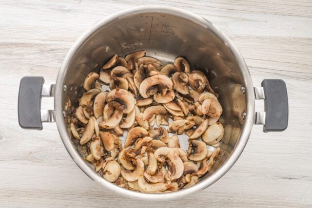 Sliced mushrooms in a stainless steel pot.
