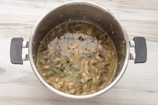 Boiling mushroom and herb mixture in a stainless steel pot.