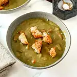 Creamy vegetable soup with croutons and salt in the background.