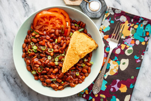 Instant Pot baked pinto beans served in a bowl with cornbread and sliced tomato.