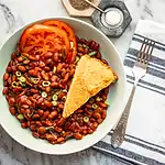 Creamy cornbread served with buttery baked beans and fresh tomato slices.