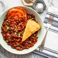Creamy cornbread served with buttery baked beans and fresh tomato slices.