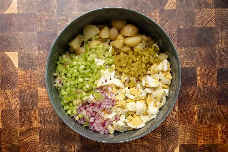 Diced potatoes, chopped celery, minced garlic, chopped hard-boiled eggs, and chopped red onions in a bowl.
